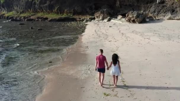 Mann und Frau spazieren bei Sonnenuntergang am tropischen Strand entlang und verfolgen Luftaufnahmen von jungen Paaren im Urlaub, die Spaß am Strand haben. Paar spaziert am leeren Strand bei Sonnenuntergang am Strand. — Stockvideo