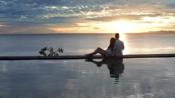 Verliebtes Paar im Luxus-Resort im romantischen Sommerurlaub. Menschen, die sich zusammen im Swimmingpool entspannen und den schönen Blick auf das Meer bei Sonnenuntergang genießen. glückliche Verliebte auf Hochzeitsreise. Beziehung — Stockvideo