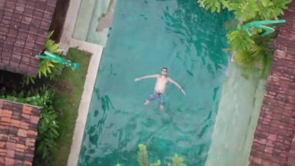 Vista aérea do drone do homem novo que flutua sobre a piscina azul que aprecia banhos de sol e férias no destino tropical. Pessoas viagens turismo férias conceito — Vídeo de Stock