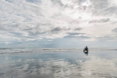 Sahilde motosiklete binen şapkalı adam. Bali plajda gün batımında Moto çapraz dirtbiker. Genç hipster erkek özgürlük ve aktif yaşam tarzı zevk, bir bisikletçiler tur eğlenmek.