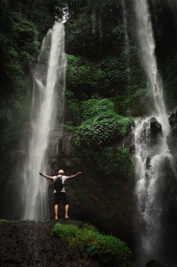 Şelalenin tadını çıkaran adam el kaldırdı. Arka plan dağ ve yağmur ormanlarında vahşi doğaya Seyahat Yaşam tarzı ve başarı kavramı tatil.