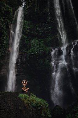 Şelale yakınındaki harika bir ormanda yoga yaparken lotus pozisyonunda meditasyon güzel genç kadın. Tropik Şelale yakınlarındaki Rock güzel kadın Pratik Yoga