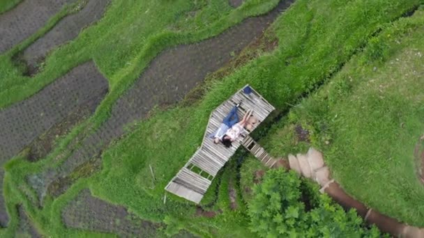 Вид зверху на повітря. Двоє закоханих молодих людей лежать на дерев'яному мосту. рисові тераси навколо молодої пари . — стокове відео