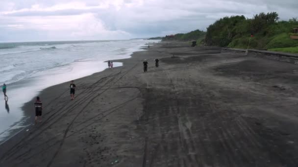 Dos hombres hipster guapos montando moderno motorista personalizado café en la playa de arena negra cerca del océano. Concepto de viaje de aventura. Punto de surf con olas del océano. Un disparo aéreo. 4k — Vídeos de Stock