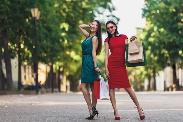 Junge attraktive Mädchen mit Einkaufstüten in der Sommerstadt. schöne Frauen mit Sonnenbrille, die in die Kamera schauen und lächeln. Positive Emotionen und Shopping Day-Konzept. — Stockfoto