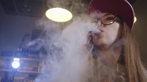 Uma jovem bonita de boné vermelho fuma um cigarro eletrônico na loja de vape. Fecha a porta. Movimento lento . — Vídeo de Stock