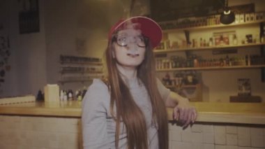 Kırmızı şapkalı genç bir kadın vape dükkanında elektronik sigara içiyor. - Yakın çekim. Yavaş çekim.