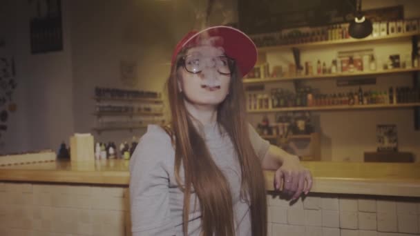 Young pretty woman in red cap smoke an electronic cigarette at the vape shop. Closeup. Slow motion. — Stock Video