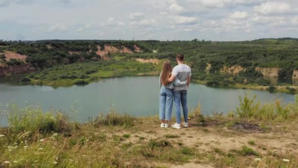 O casal está em pé num penhasco junto ao lago. Casal apaixonado abraçando contra o pano de fundo de belas vistas da natureza. Aéreo. 4K — Vídeo de Stock