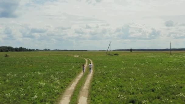 Vue Aérienne D'un Couple Ludique Tenant La Main Et Courir Sur La Route Rurale. La caméra est devant eux. Coup 4K .