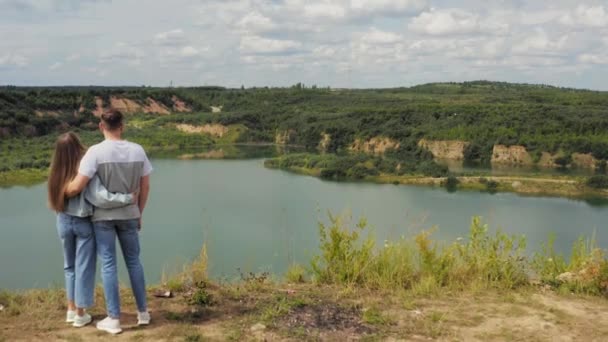 O casal está em pé num penhasco junto ao lago. Casal apaixonado abraçando contra o pano de fundo de belas vistas da natureza. Aéreo. 4K — Vídeo de Stock