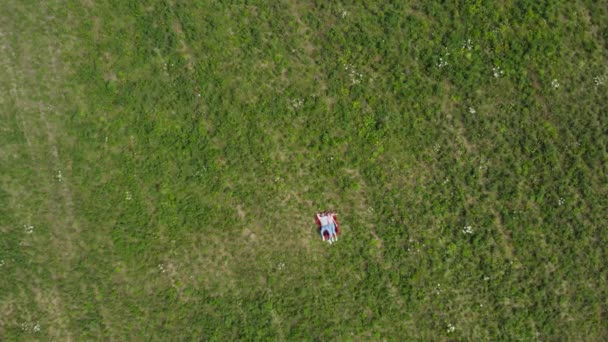 Glückliches junges Paar auf dem Gras auf der Wiese liegend. fliegt die Kamera langsam auf sie zu. von oben nach unten. 4k. — Stockvideo