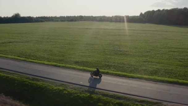 El hombre monta una motocicleta en una carretera de campo al atardecer disparo aéreo de rastreo de drones. 4K . — Vídeo de stock