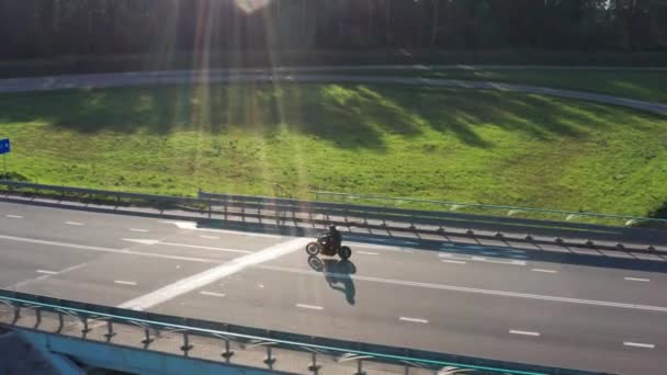 El hombre en motocicleta conduce a través de un cruce al atardecer. Disparo aéreo de rastreo de drones. 4K . — Vídeo de stock