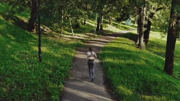 Joven chica atractiva corriendo en el parque de la ciudad. Mujer corriendo en vista trasera aérea de madera. 4K, tiro de seguimiento . — Vídeos de Stock