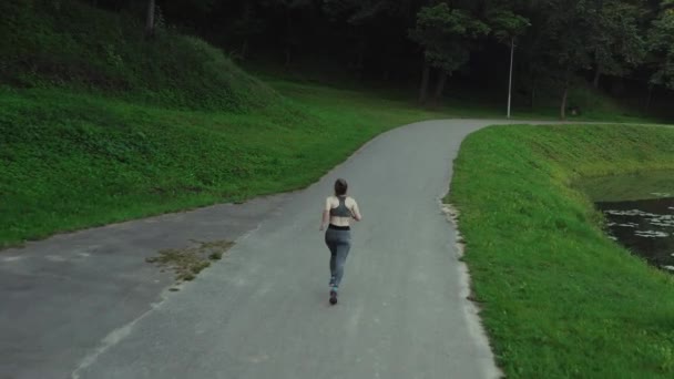 Joven chica atractiva corriendo en el parque de la ciudad. Mujer corriendo en vista trasera aérea de madera. 4K, tiro de seguimiento . — Vídeos de Stock