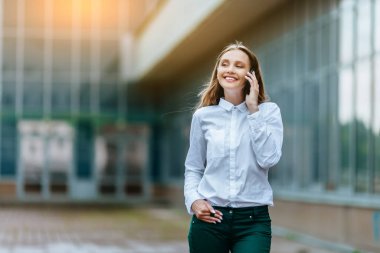 Genç famale akıllı telefon arıyor. Çekici iş kadını telefonla konuşuyor. Ofis binası Arka Plan. Teknoloji internet ve mutlu insanlar kavramı.