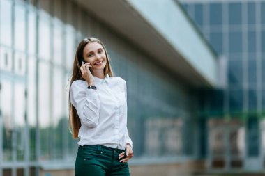 Genç famale akıllı telefon arıyor. Çekici iş kadını telefonla konuşuyor. Ofis binası Arka Plan. Teknoloji internet ve mutlu insanlar kavramı.