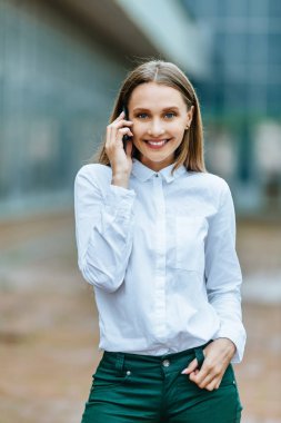 Genç famale akıllı telefon arıyor. Çekici iş kadını telefonla konuşuyor. Ofis binası Arka Plan. Teknoloji internet ve mutlu insanlar kavramı.