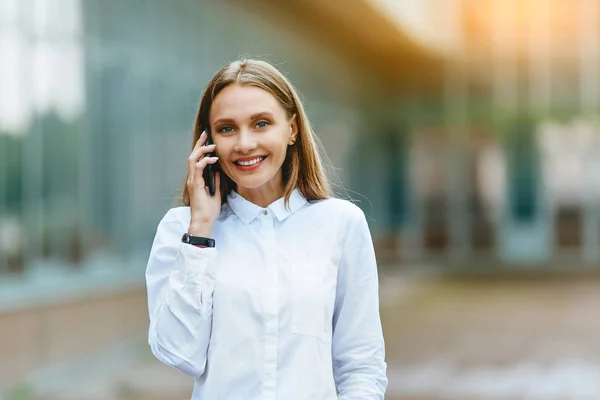 Young famale calling on a smartphone. Attractive businesswoman talking by phone. Office building Background. Technology internet and happy people concept. — Stock Photo, Image