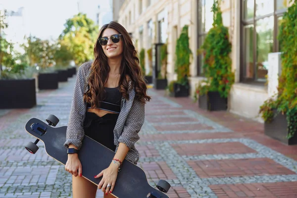 Schöne junge Frau mit Longboard auf der Stadtstraße bei sonnigem Wetter. junges Hipster-Mädchen posiert mit Longboard, Skateboard, Streetphoto, Lebensstil, Freiheit, glücklichem Gesicht. — Stockfoto