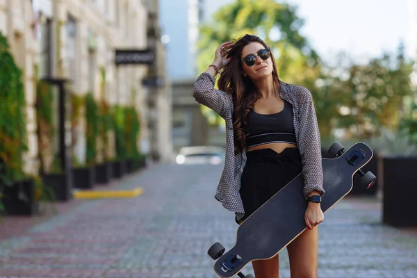 Schöne junge Frau mit Longboard auf der Stadtstraße bei sonnigem Wetter. junges Hipster-Mädchen posiert mit Longboard, Skateboard, Streetphoto, Lebensstil, Freiheit, glücklichem Gesicht. — Stockfoto