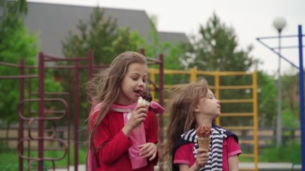 Crianças felizes comendo sorvete ao ar livre no parque infantil. Dia ventoso de verão. O bloqueio e a quarentena terminaram . — Vídeo de Stock