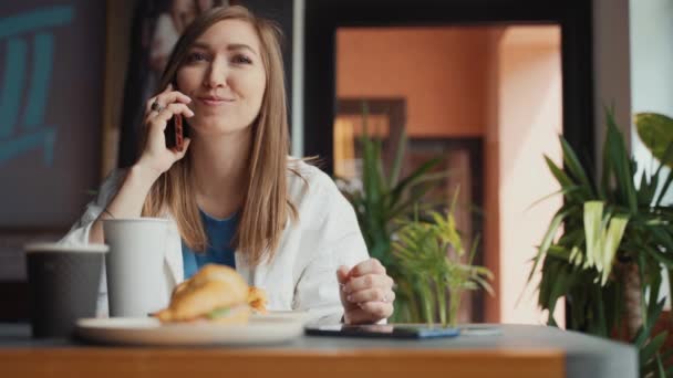 一个年轻的女人正坐在咖啡店里用手机交谈. — 图库视频影像