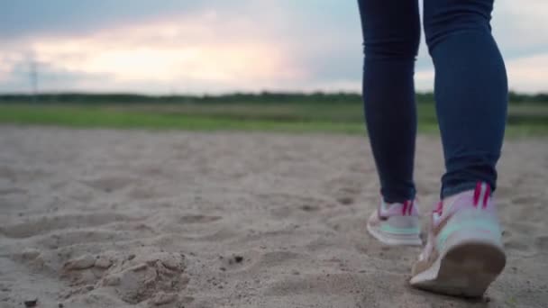 Nærbilde av kvinneføtter i joggesko tråkker over sand ved solnedgang. – stockvideo