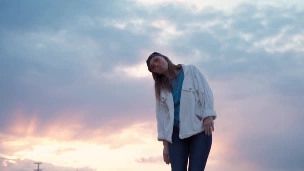 Joven hermosa mujer bailando al atardecer. Día cálido y luz de fondo suave. Chica bonita en la tapa relajante durante las vacaciones de verano . — Vídeo de stock