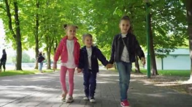 Parkta el ele tutuşan üç çocuk. İki kız ve oğlanın güzel yaz gününün tadını çıkardığı ön manzara..