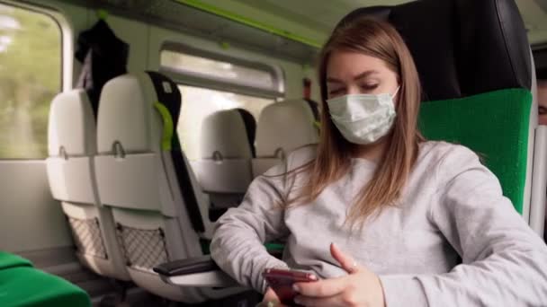Solunum Maskeli Genç Kadın Trendeki Akıllı Telefonu Kullanıyor. Şehirde insan taşımacılığı. Önlem olarak sosyal uzaklık, artan risk. — Stok video