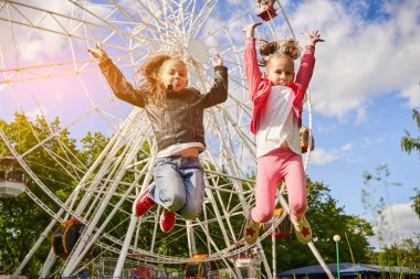 İki kız lunaparkta eğleniyor. Arka planda dönme dolap var..