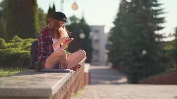 Étudiant utilisant un smartphone sur le campus. Belle jeune étudiante assise près de l'Université et utilisant un smartphone. Heure avancée du coucher du soleil. — Video