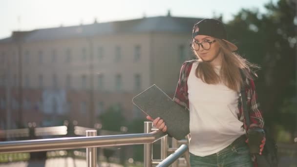 Boldog fiatal lány diák öltözött alkalmi ruhát egy csésze kávét és hátizsák a háta mögött sétál a városban. Női diák laptoppal és kávét iszik. Nyári naplemente.