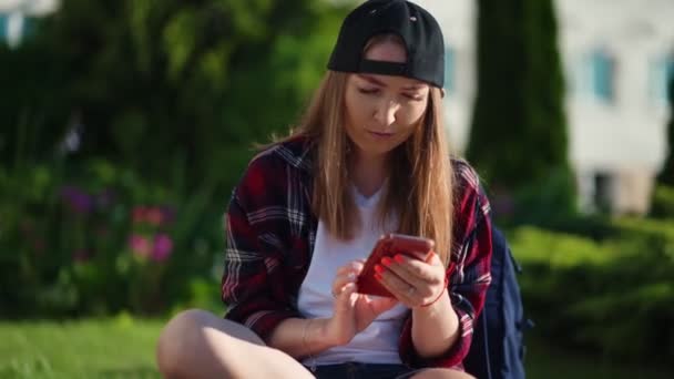 Vysokoškolák používající smartphone v kampusu. Krásná mladá studentka sedící poblíž univerzity a používající smartphone. Letní západ slunce. — Stock video