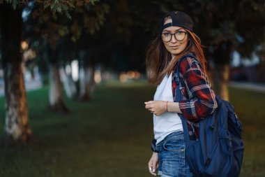Sırtında bir fincan kahve ve sırt çantasıyla gündelik giysiler içinde şehirde dolaşan mutlu genç kız öğrenci. Dizüstü bilgisayar tutan ve kahve içen bir kadın öğrenci. Yaz gün batımı.