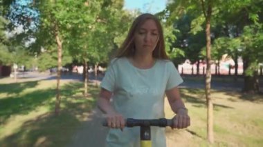 Kız gün batımında şehir parkında elektrikli scooter ya da e-scooter kullanıyor. Şehir parkında elektrikli taşıma kullanan kadın