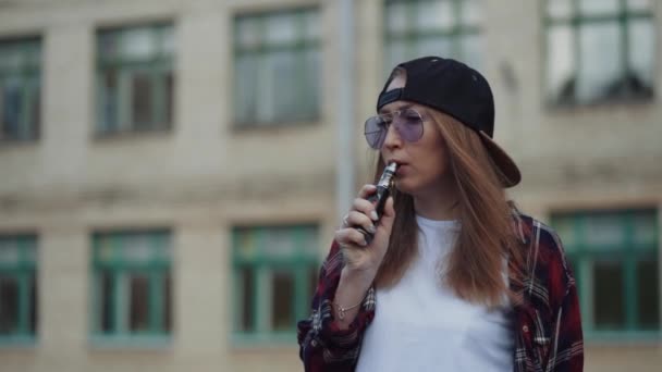 Close-up hübsche junge Hipster-Frau mit schwarzer Mütze vape ecig. Mädchen vape beliebte ecig Gadget, vaping device.Happy Brünette vaper Mädchen mit e-cig. Porträt eines weiblichen Rauchers mit elektronischer Zigarette — Stockvideo