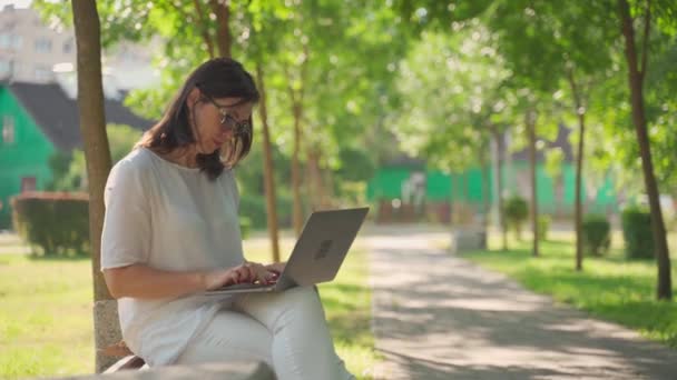 아름다운 사업 수석 부인이 안경을 쓰고 야외 공원에 앉아 노트북을 사용하며 즐겁게 일하고 있다. 현대 여성, 새로운 세대. 건강하고 명랑 한 은퇴 한 여성. 나이에 대한 개념 — 비디오