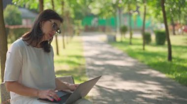 Neşeli, tapılası, güzel bir iş kadını, gözlüklü, parkın dışında oturan, dizüstü bilgisayarı üzerinde çalışan. Modern kadın, yeni nesil. Sağlıklı, neşeli, yaşlı, emekli bayan. Yaş kavramı