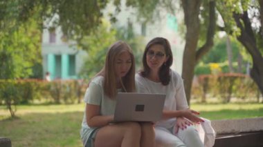 Genç bir kadın, emekli annesine laptopuyla parkta otururken yardım ediyor. Yaş Kapsayıcılığı kavramı