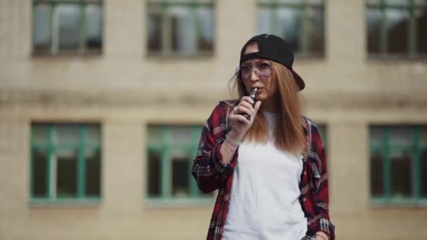 Ładna młoda hipsterka w czarnym ecygarze z kapturkiem. Dziewczyna vape popularne ecig gadżet, vaping urządzenia.Happy brunetka vaper dziewczyna z e-cig. Portret palaczki modelki z papierosem elektronicznym — Wideo stockowe