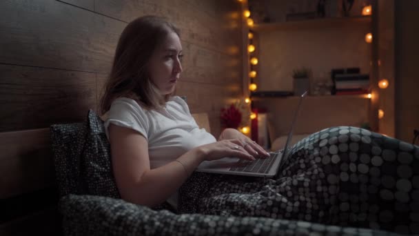Eine lächelnde, zufriedene junge Frau spricht mit einem Video, in dem sie ihren Laptop zu Hause im Bett benutzt. Technologie, Internet, Kommunikation und Menschen-Konzept . — Stockvideo