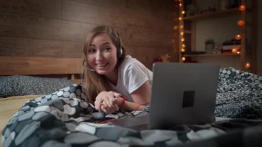 Güzel, çekici genç bir kadın yatakta uzanıyor ve sosyal medyayı kullanmak ve online alışveriş yapmak için bilgisayar laptopu üzerinde çalışıyor rahat bir yatak odasında evinde dinleniyor. Ev kavramından çalış.