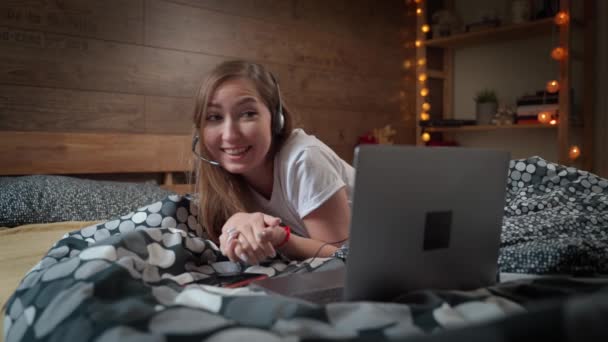 美しい魅力的な若い女性がベッドの上に横たわって、ソーシャルメディアやオンラインショッピングを使用するためのコンピュータのラップトップで働いて居心地の良いベッドルームで自宅でリラックスします。家のコンセプトからの仕事. — ストック動画