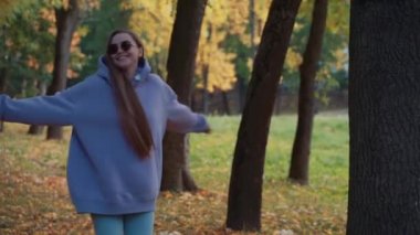 Güz parkında pembe kapüşonlu giyinmiş güzel, mutlu bir kadın dans ediyor. Mevsim ve insanlar kavramı. Doğa, ağır çekim.