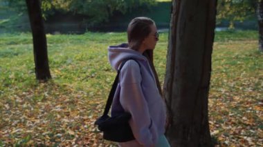 Güz parkında pembe kapüşonlu güzel, mutlu, gülümseyen genç bir kadının yan görüntüsü. Mevsim ve insanlar kavramı. Doğa, ağır çekim.