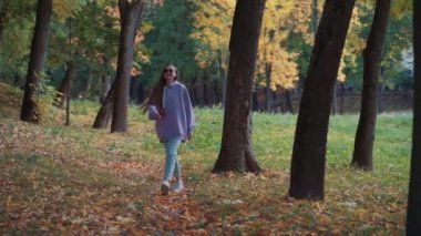 Sonbahar parkında pembe kapüşonlu güzel, mutlu, genç bir kadın yürüyor. Mevsim ve insanlar kavramı. Doğa, ağır çekim.