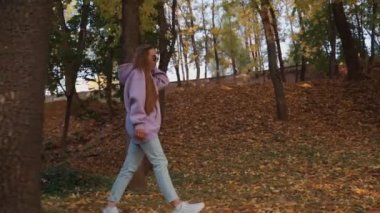 Güz parkında pembe kapüşonlu güzel, mutlu, gülümseyen genç bir kadının yan görüntüsü. Mevsim ve insanlar kavramı. Doğa, ağır çekim.